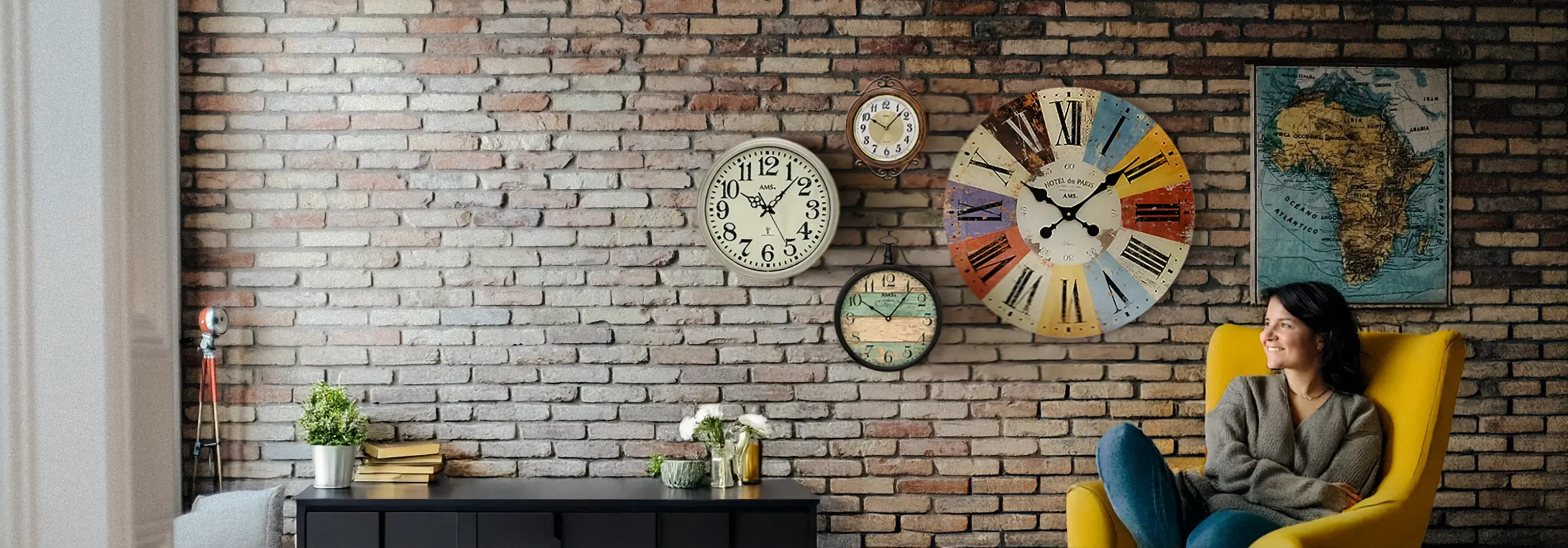 Frau auf gelbem Stuhl vor Ziegelwand mit Wanduhren