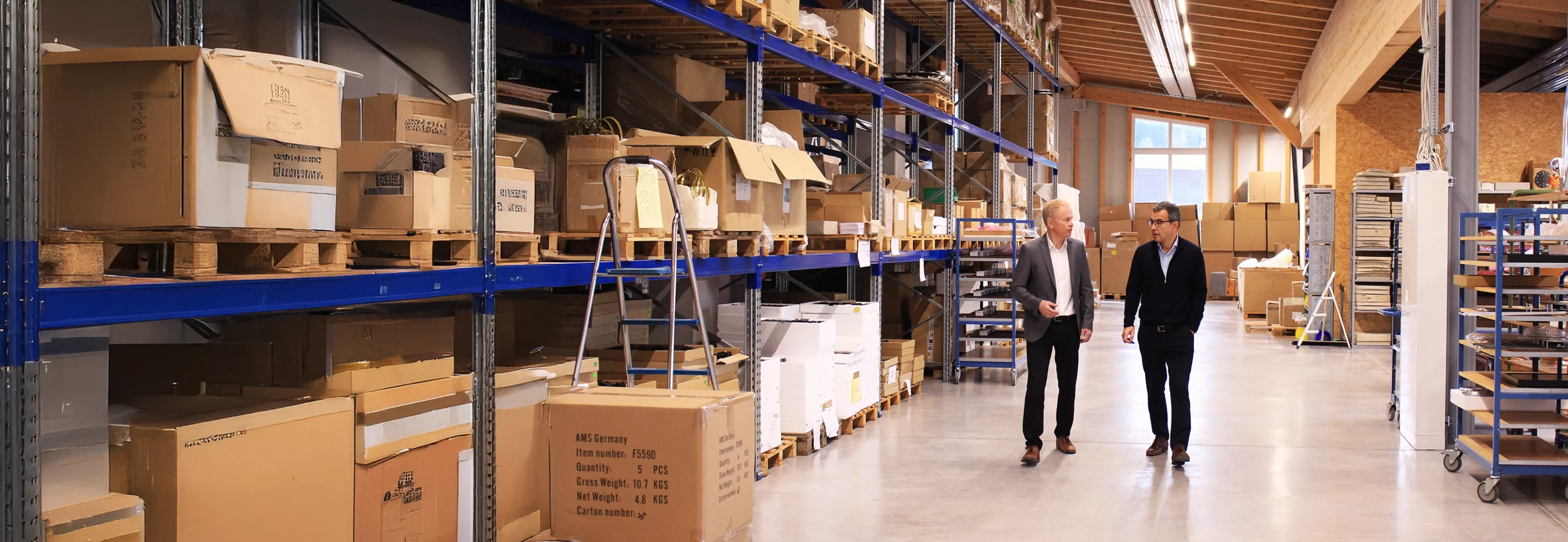 Männer gehen durch ein Lager voller Kartons und Regale